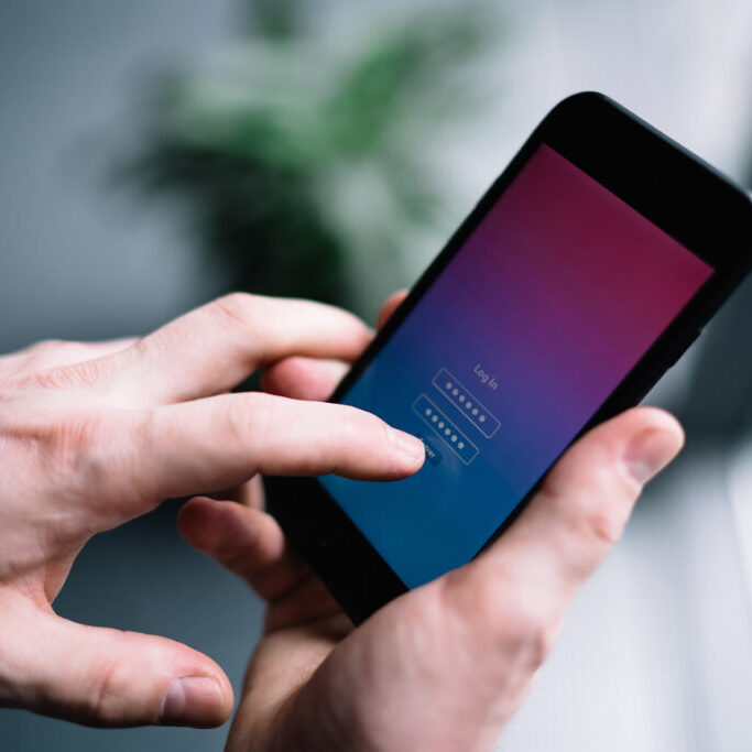 Close-up of a person holding a smartphone and entering a password on a login screen with a gradient background.