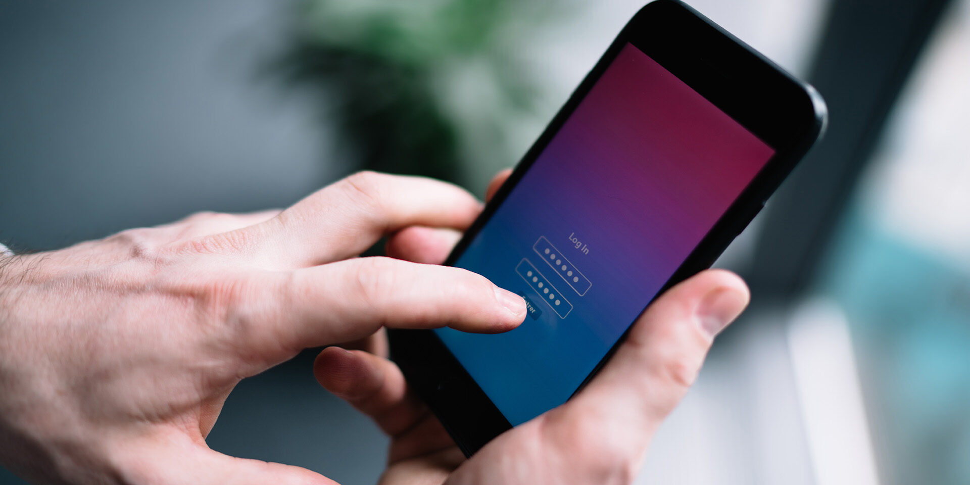 Close-up of a person holding a smartphone and entering a password on a login screen with a gradient background.