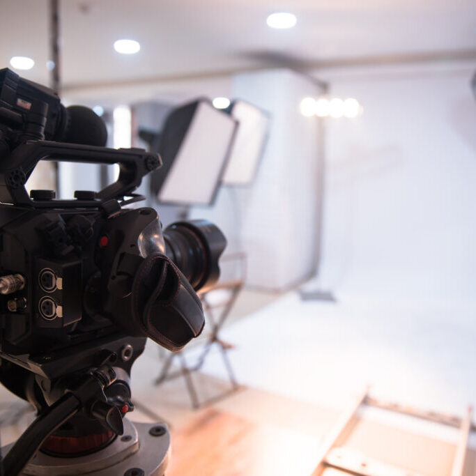 Professional video camera set up in a well-lit studio with softboxes and background lights prepared for a photo or video shoot.